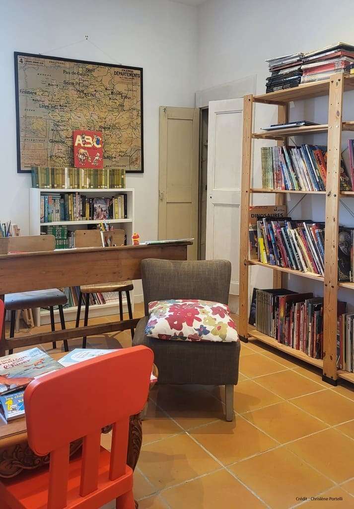 Espace lecture de la bibliothèque de Saint-Hilaire d’Ozilhan avec fauteuil et étagères de livres